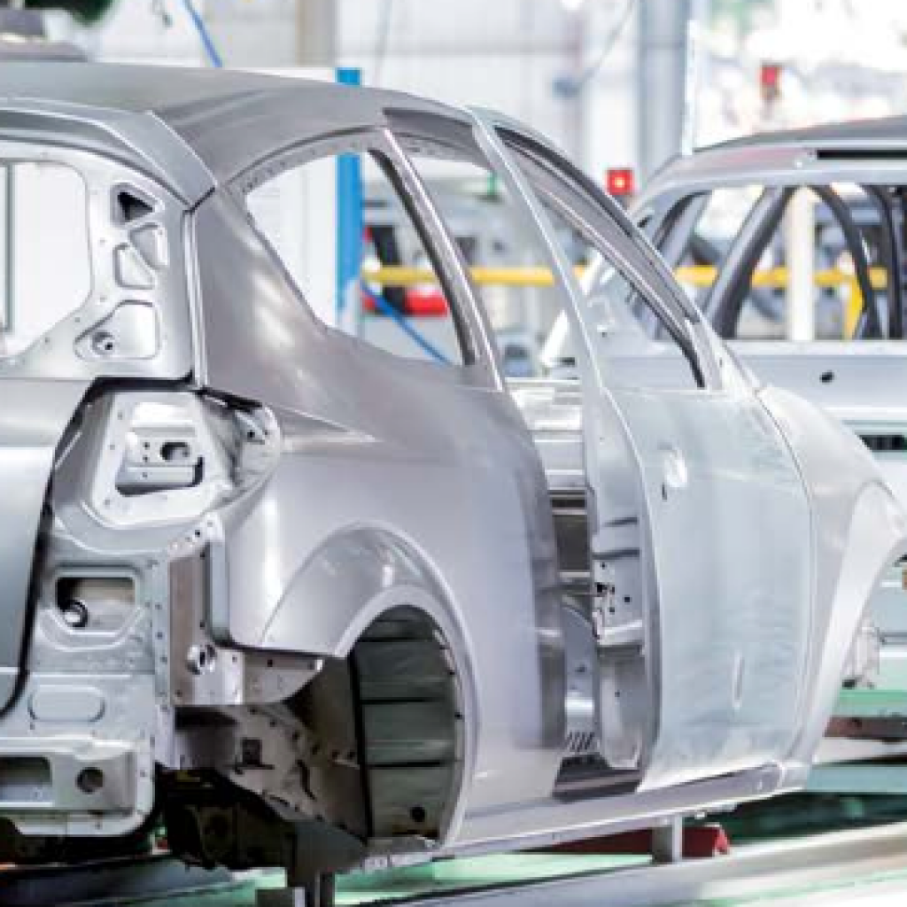 Carcasa metálica de un coche sin pintar en una línea de producción industrial, en tonos plateados y grises, con un ambiente de fábrica serio